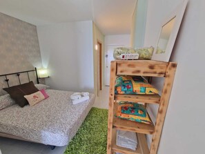 A bedroom with a bed, a wooden shelf with folded clothes, a bedside table with a lamp, and a wall-mounted mirror. - APARTMENT YELLOW SEA 173 (Empuriabrava)