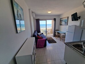 A compact living space with a sofa, a dining table, a kitchen area, and a view of the sea through a glass door. - BLUE SEA APARTMENT. (Empuriabrava)