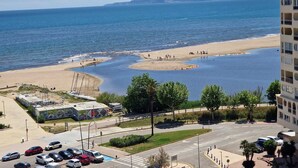 Kystudsigt med strand, parkeringsområde og en bygning med altaner.