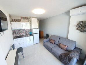 A compact living space with a kitchenette, a grey sofa with patterned cushions, a small table, and a chair. - APARTMENT BRUEL 17-12. (Empuriabrava)