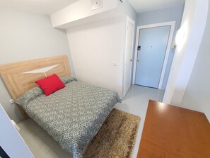 A bedroom with a wooden headboard, a patterned bedspread, a red pillow, a brown rug, and a wooden table. - APARTMENT BRUEL 17-12. (Empuriabrava)
