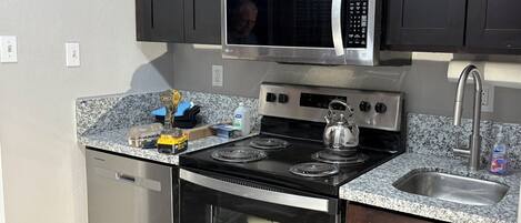 Une cuisine compacte équipée d’un four à micro-ondes encastré, d’une cuisinière, d’un four et d’un évier en acier inoxydable.