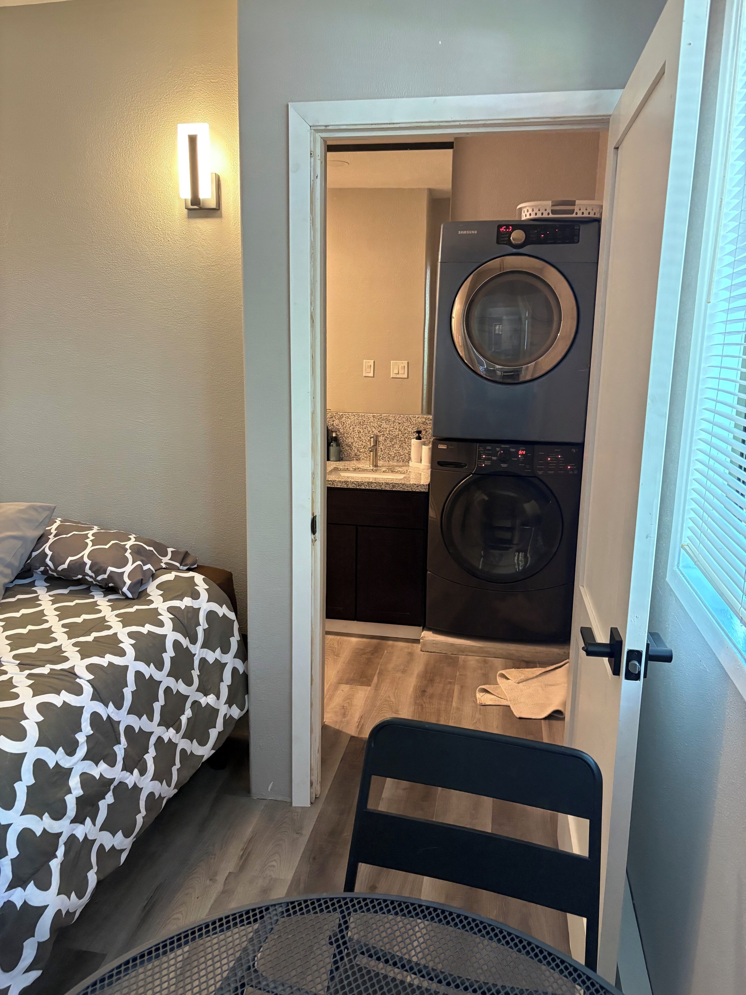 A bedroom with a bed, a chair, and a laundry area with a washing machine and dryer.