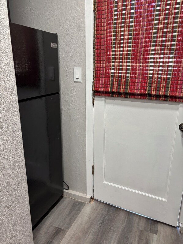 A kitchen with a black refrigerator, a white door, and a red plaid window blind.