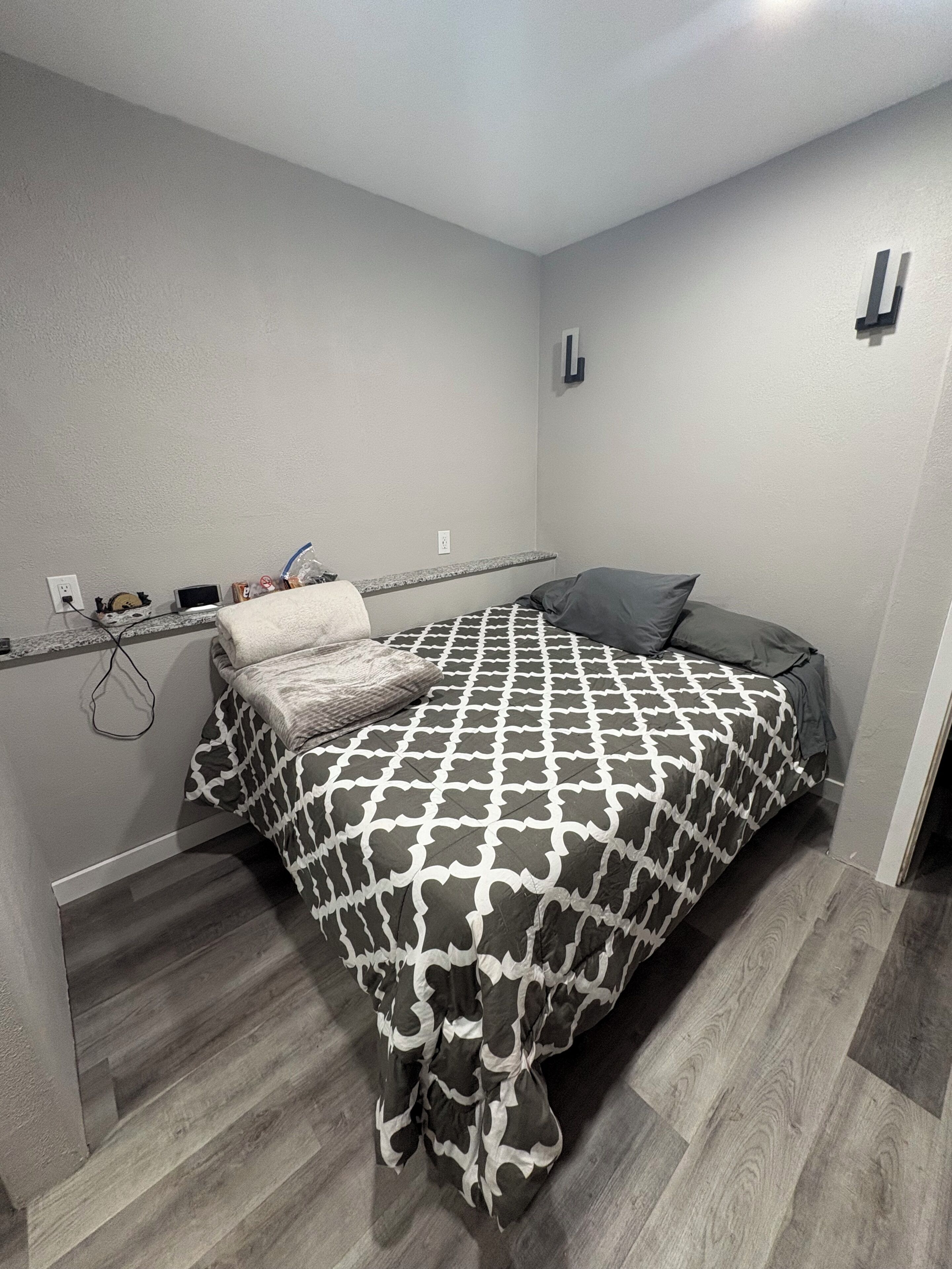 Un dormitorio con una cama, una mesita de noche, un enchufe y una toma de corriente.