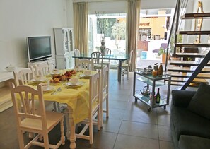 A dining area with a table set for four, chairs, a television, and a kitchen area in the background.