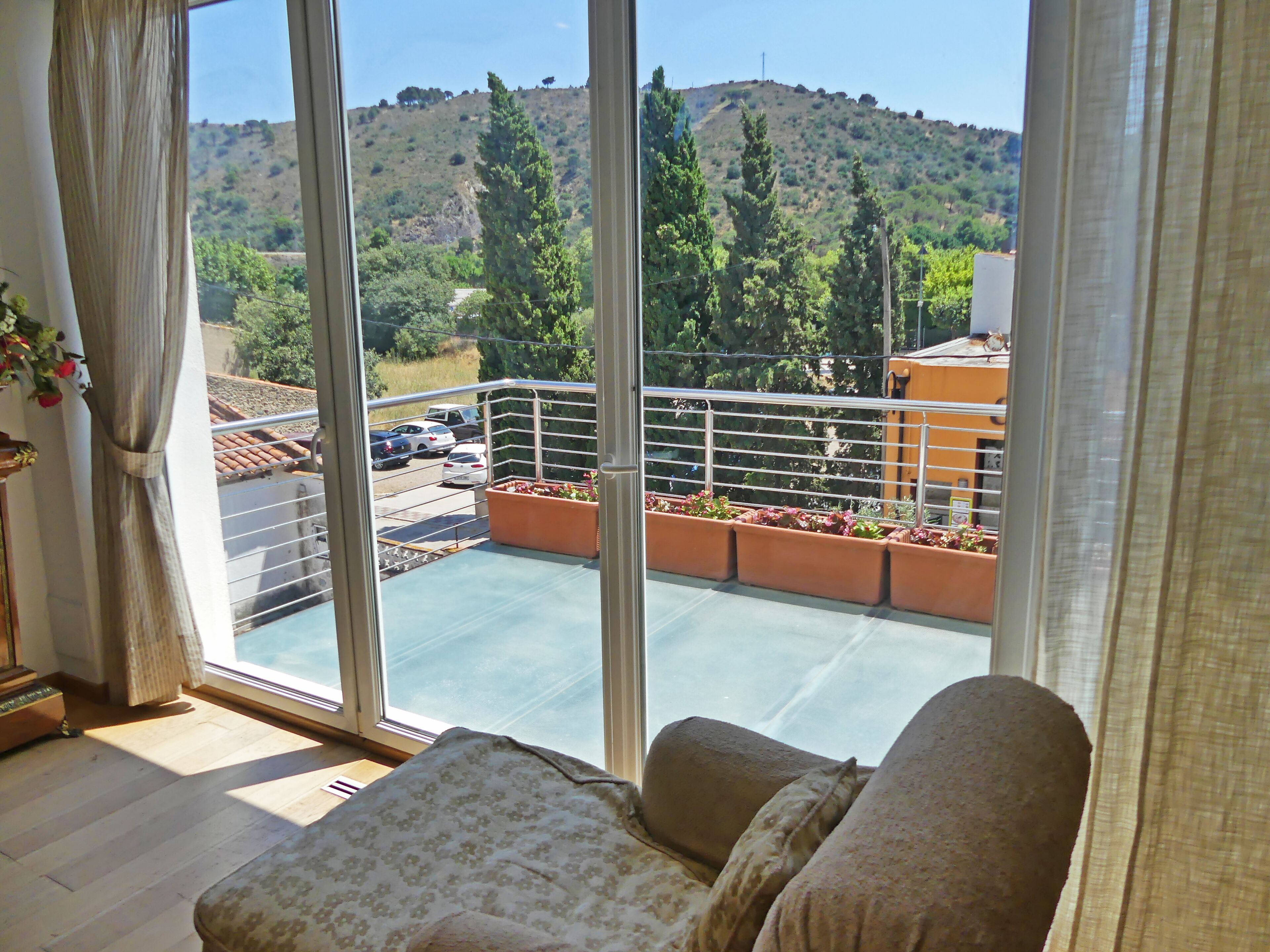A balcony with a view of a hilly landscape, a railing, and a seating area with cushions.
