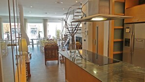 A modern kitchen with a glass countertop, stainless steel appliances, and a view of the dining area.