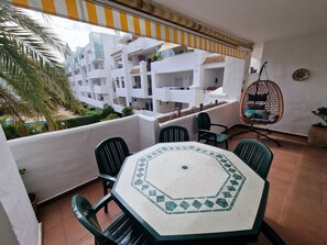 Ein Balkon mit Tisch und Stühlen, einem Hängesessel und Blick auf weiße Gebäude.