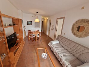Un salon comprenant un canapé, un téléviseur, une table à manger avec des chaises, une table basse et un miroir décoratif.
