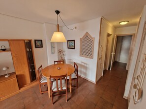 Un coin repas comprenant une table ronde en bois, des chaises, une lampe suspendue et une horloge murale.