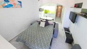 A compact room with a bed, a desk, a chair, a TV, and a kitchenette in the background. - GRISLAND POOL STUDIO (Roses)