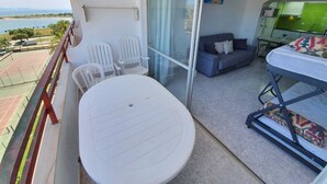 A balcony with a table and chairs, a sofa, a bed, and a view of the sea. - GRISLAND POOL STUDIO (Roses)
