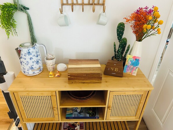 Ein Holztisch mit einer Uhr, einer weißen Tasse, einem floralen Wasserkocher, einem Kaktus und einer Vase mit Blumen.