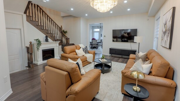 A living room with a fireplace, leather sofas, a chandelier, and a staircase. - Modern Oakville Home | 2 King, 2 Queen + Gazebo (Oakville)