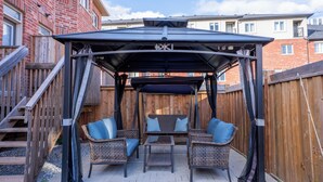 A covered patio area with wicker furniture and a swing. - Modern Oakville Home | 2 King, 2 Queen + Gazebo (Oakville)