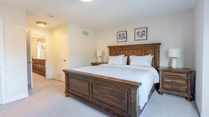 A bedroom with a large wooden bed, two bedside tables with lamps, a door leading to another room, and two framed pictures on the wall. - Modern Oakville Home | 2 King, 2 Queen + Gazebo (Oakville)