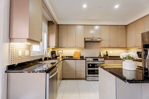 A modern kitchen with stainless steel appliances, a central island, and a dot-patterned backsplash. - Modern Oakville Home | 2 King, 2 Queen + Gazebo (Oakville)