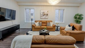 A modern living room with a large flat-screen TV, leather sofas, a chandelier, and a potted plant. - Modern Oakville Home | 2 King, 2 Queen + Gazebo (Oakville)