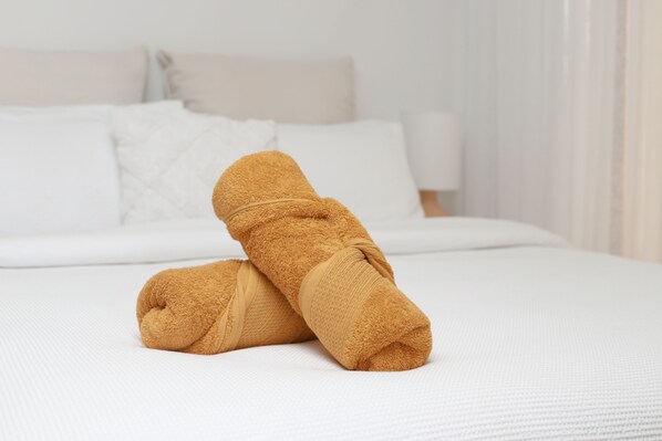 A neatly made bed with white linens and a rolled towel placed on it.