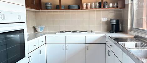 A modern kitchen with white cabinets, a built-in oven, a microwave, a sink, and a window.