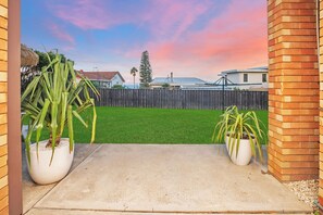 A concrete patio with two potted plants, a wooden fence, and a grassy yard.