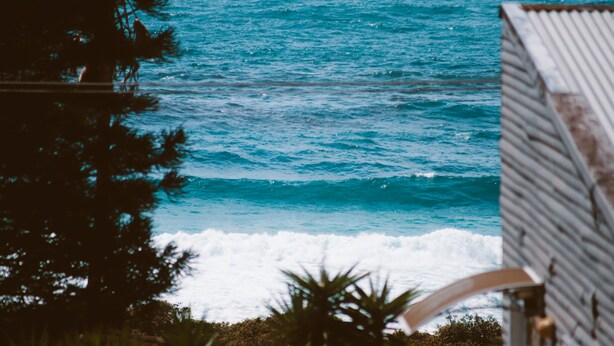 Une vue sur la côte, avec des vagues, un bâtiment doté d’un toit en tôle ondulée et une végétation luxuriante.