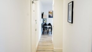Un couloir avec un plancher en bois, des murs blancs, une porte à gauche et un tableau encadré à droite.