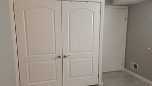 Een gesloten, witte dubbele deur met een eenvoudig handvat, een effen muur en een lichtkleurige houten vloer.