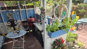 Een terras met een ronde tafel, stoelen, een barbecue en diverse potplanten.
