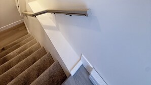 Una escalera con barandilla, peldaños alfombrados y pared blanca.