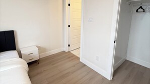 Un dormitorio con cama, mesita de noche, radiador, armario y una puerta que da a otra habitación.