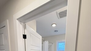 Un pasillo con una puerta blanca, una cortina de ducha y una ventana con vista a una casa.