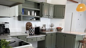 Una cocina moderna con armarios verdes, encimera de granito, cafetera y lámpara colgante.