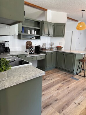 Een moderne keuken met groene kastjes, een granieten aanrecht, een koffiezetapparaat en een hanglamp.