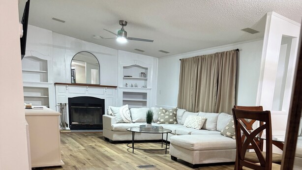 Una sala de estar con chimenea, sofás blancos, una mesa de centro y piso de madera.