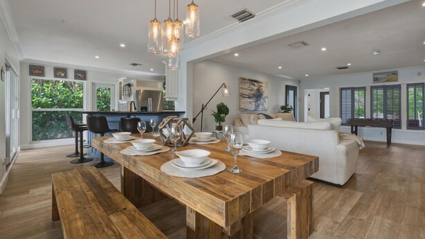 A spacious dining area with a wooden table set for six, a white sofa, and a kitchen in the background. - Fox Isles Luxury Waterfront With Pool Near Beach (Fort Lauderdale)