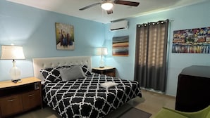 A bedroom with a bed, two bedside tables, a chair, a ceiling fan, and artwork on the walls. - Family Friendly 8-bedroom house in Cataño, Up to 30+ Guests (Cataño)