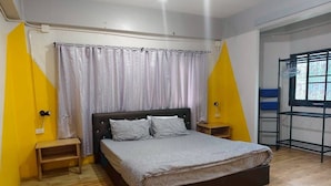A bedroom with a bed, wooden nightstands, a window with a view, and a door. - New Me U Hostel (Chiang Mai)