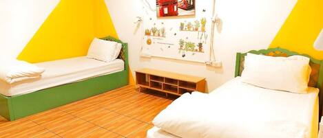 A room with two beds, a wooden floor, and a wall with a picture and small potted plants.