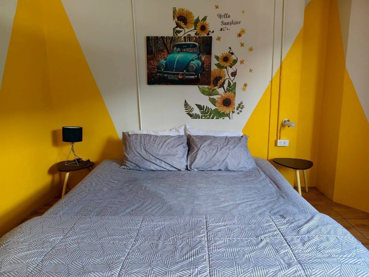 A bed with patterned bedding, a wall-mounted picture, and a sunflower decoration.
