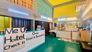 A hostel interior with a check-in counter, food and smoothie station, and a seating area. - New Me U Hostel (Chiang Mai)