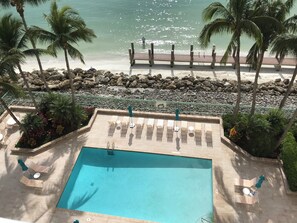 Uma área de piscina com espreguiçadeiras, um deck de madeira e vista para a praia.