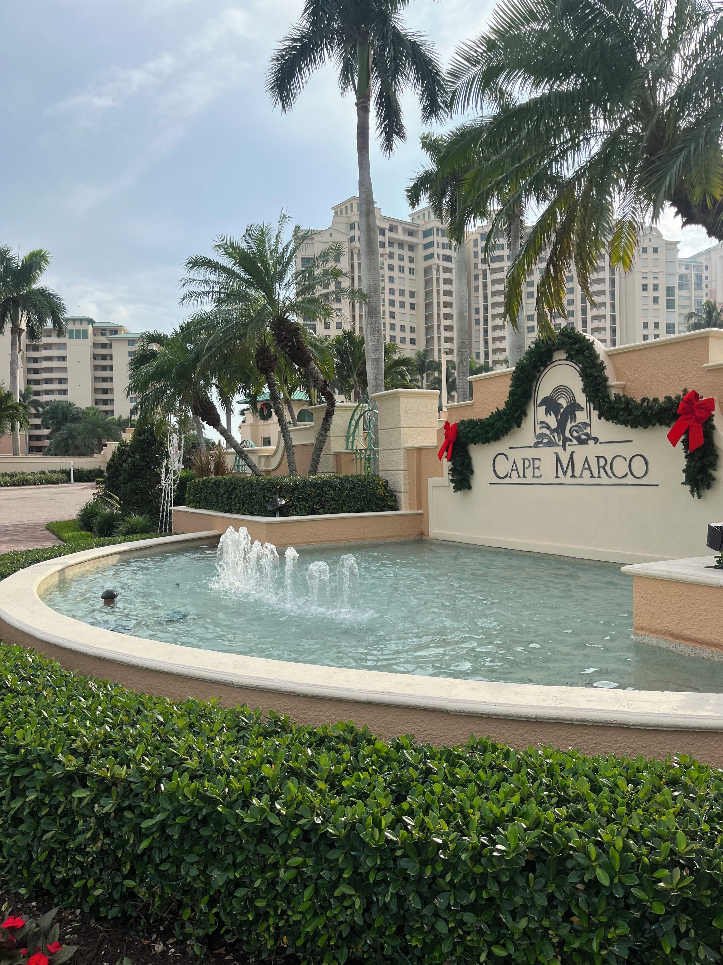 A fountain with water jets, palm trees, and a building with 'Cape Marco' signage.