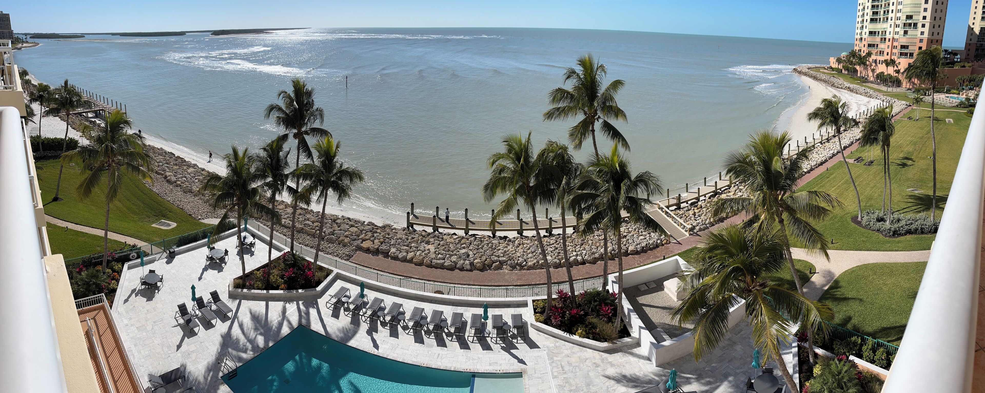 Un resort con piscina, sillas de descanso, palmeras y vista al océano.