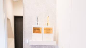 A bathroom with a mirror, two white shelves, and three bottles labeled 'SHAMPOO,' 'CONDITIONER,' and 'BODY WASH.'