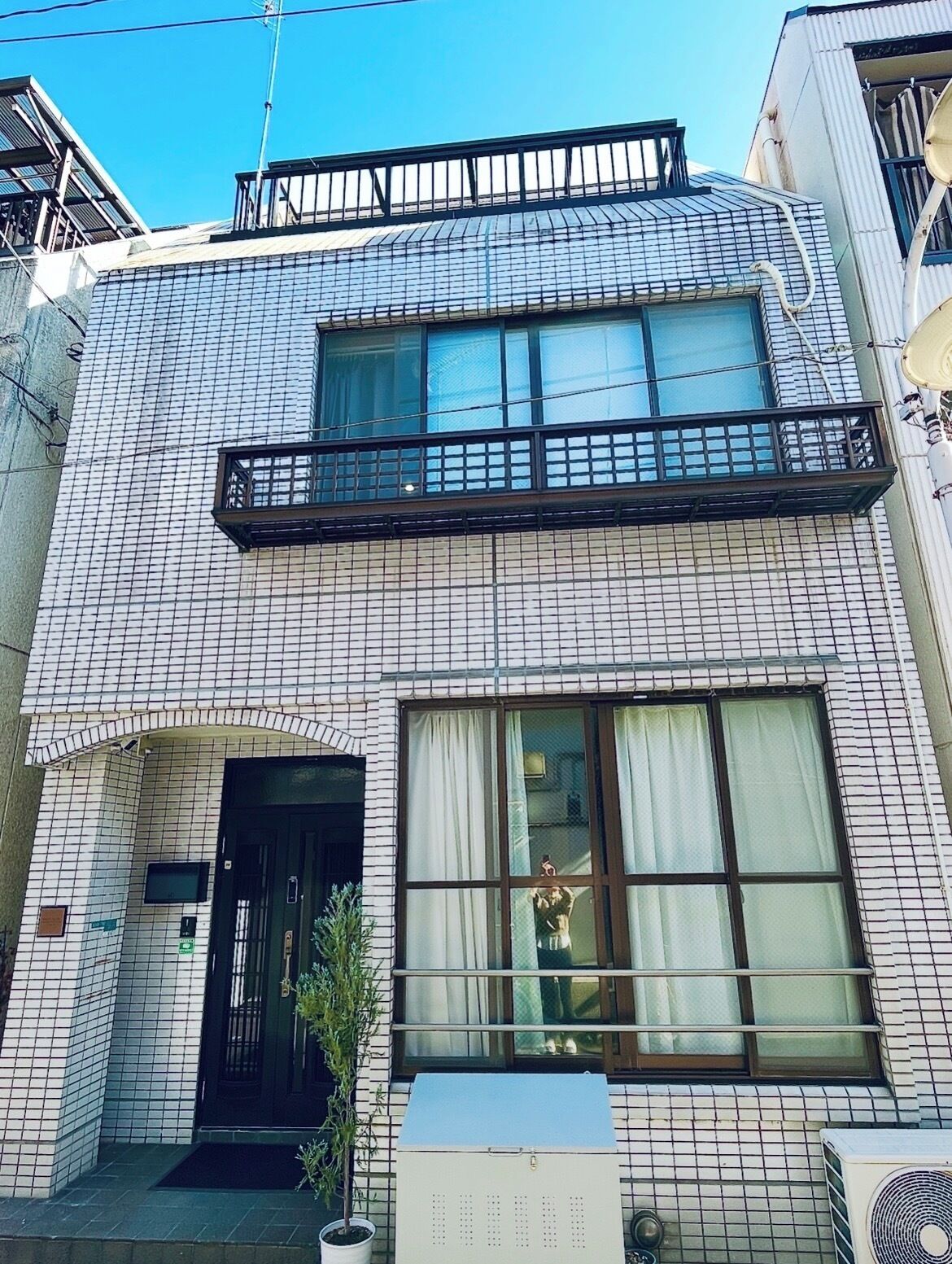 A building with a tiled facade, a black door, a window with curtains, and a small balcony.