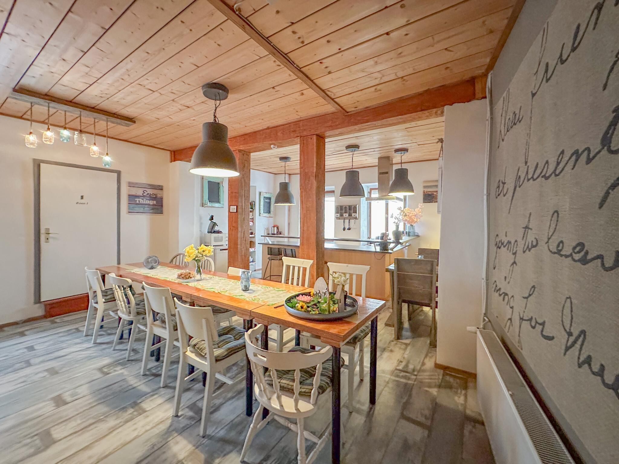 Un espace repas avec une table et des chaises en bois, un éclairage suspendu et une vue sur la cuisine.