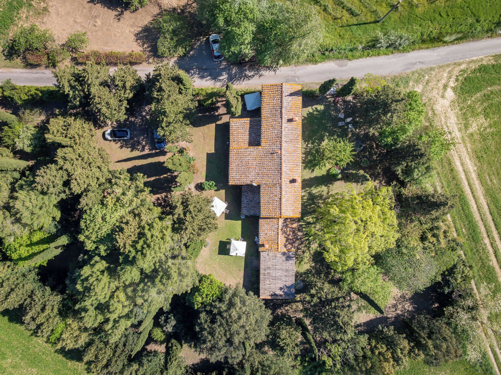 Vista aérea de una casa con un techo grande, rodeada de árboles frondosos y un cielo despejado.
