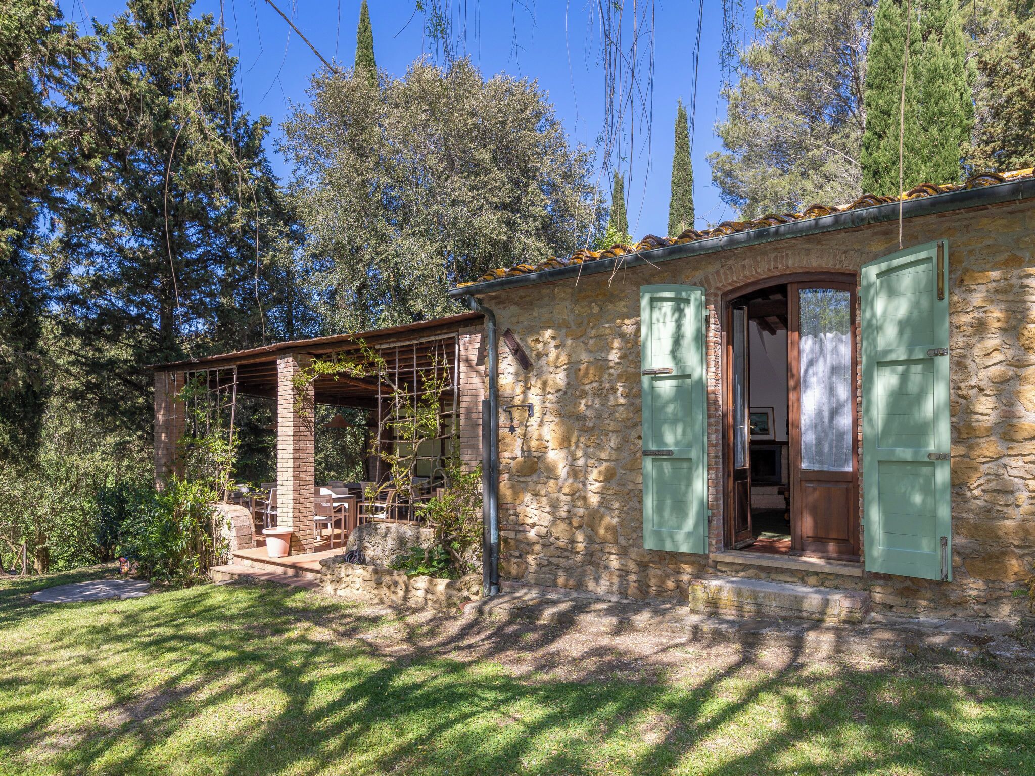 Une maison en pierre avec un patio couvert, une porte en bois et un volet vert.